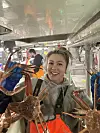 Ung arbeidar i arbeidsklede held fleire snøkrabbar inne i fabrikk på fiskebåt.