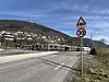 Fartsgrenseskilt på 30 km/t ved vegkant med bygningar og fjell.