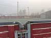 Eit innhegna ballfelt med raude plankar og grå metallgjerde i tåkete omgjevnader.