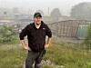 Ein mann står i graset ved eit inngjerda idrettsanlegg i tåkete ver.