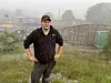 Ein mann står i graset ved eit inngjerda idrettsanlegg i tåkete ver.